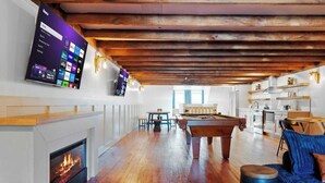 Amplia sala de estar con mesa de billar, chimenea y televisor con pantalla de inicio.