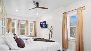 A bedroom with a bed, a ceiling fan, a TV on the wall, and a window with curtains. - The Grand Pocono Getaway Waterparks & Raceway! (Pocono Summit)