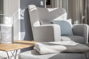 Een moderne kamer met een grijze gestoffeerde fauteuil, een houten bijzettafeltje en een glazen vaas.