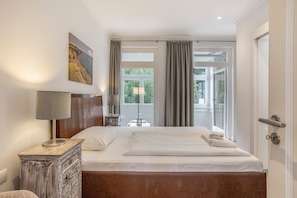 Een hotelkamer met een bed, een bureau, een lamp, een schilderij en uitzicht op groen.