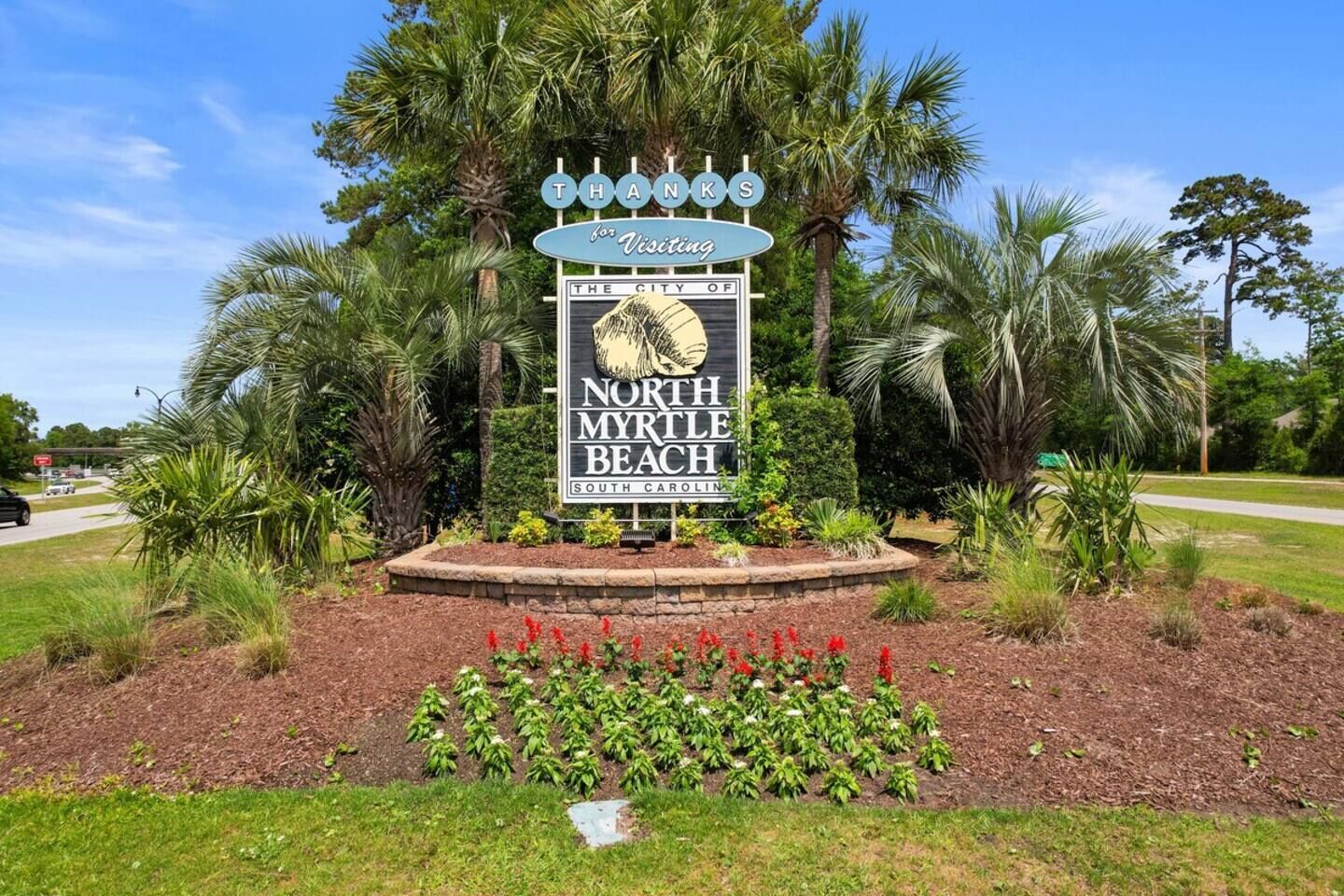 A sign for North Myrtle Beach with a palm tree and a flower bed in the foreground.