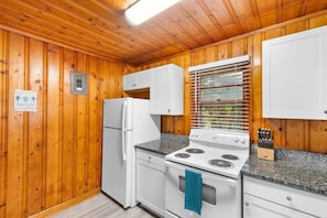 A compact kitchen with wooden walls, a white refrigerator, a stove, and a window with blinds. - 2 Bdrm Beach Cottage- Fire pit, 3 blocks to beach (North Myrtle Beach)