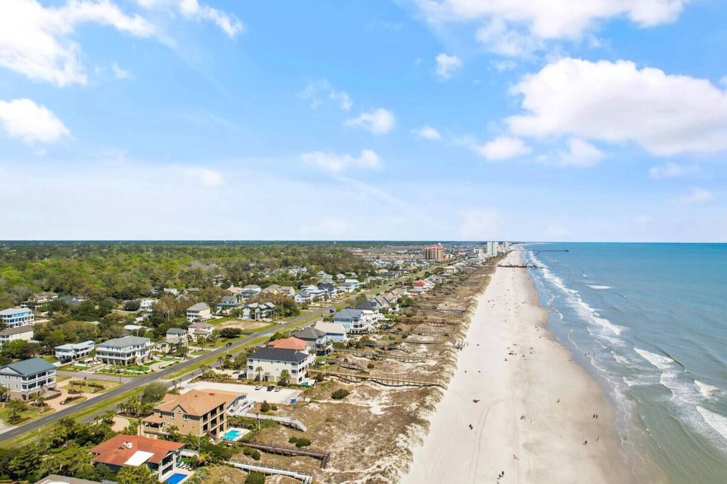 A coastal residential area with houses, a beach, and a clear sky.