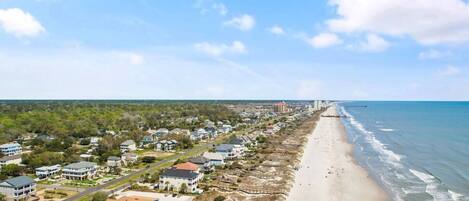 A coastal residential area with houses, a beach, and a clear sky.