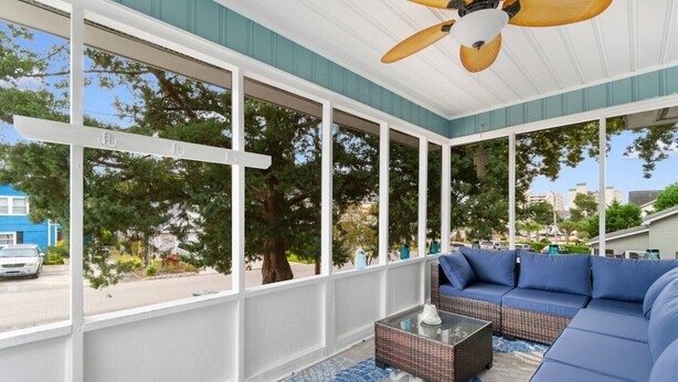 Eine überdachte Veranda mit Deckenventilator, großen Fenstern, einem blauen Sofa und einem Glastisch.