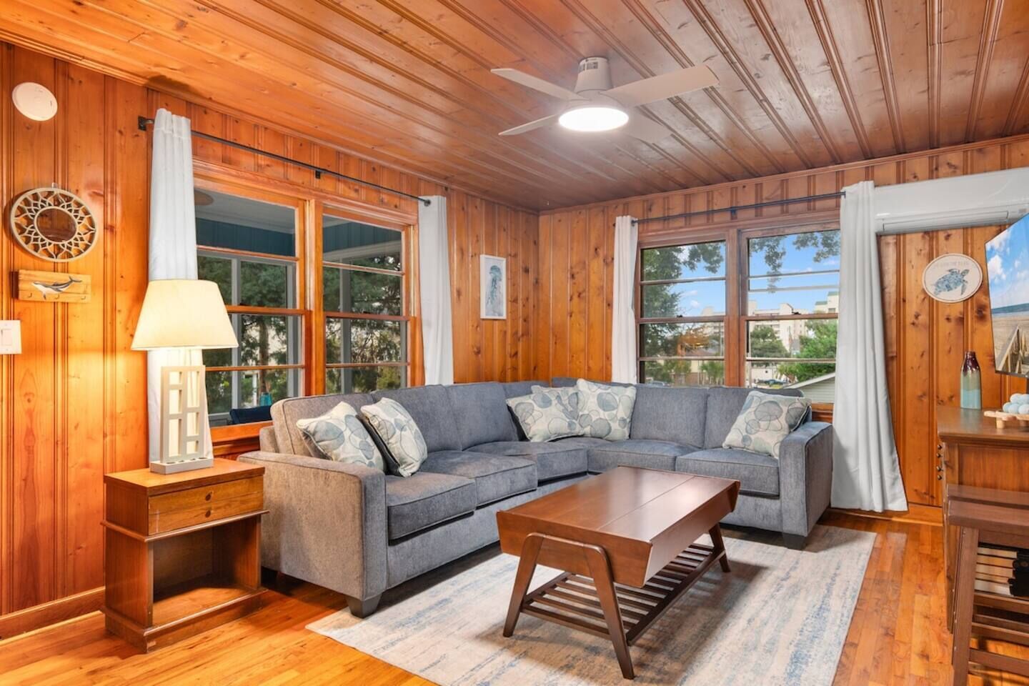 A cozy living room with a sectional sofa, wooden flooring, and large windows.