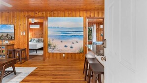 Ein Zimmer mit Holzwänden, einem großen Strandbild, einem Bett, einem Schreibtisch und einem Sessel.