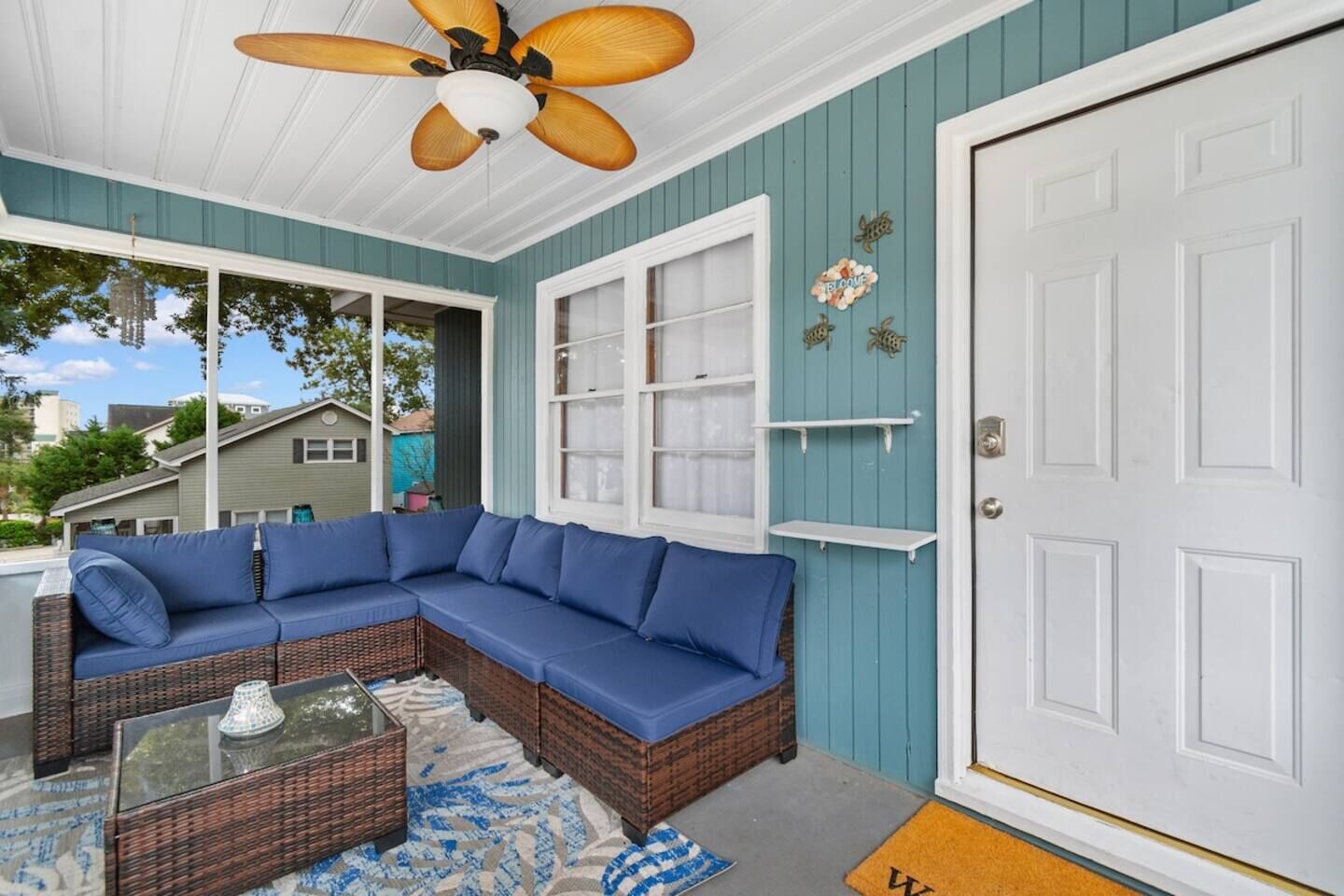 A covered porch with a sectional sofa, a glass-top coffee table, and a ceiling fan.