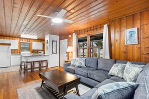 A cozy cabin interior with a wooden ceiling, a dining area, a living room with a sofa and coffee table, and a kitchen with white cabinets. - 2 Bdrm Beach Cottage- Fire Pit, 3 Blocks to Beach (North Myrtle Beach)