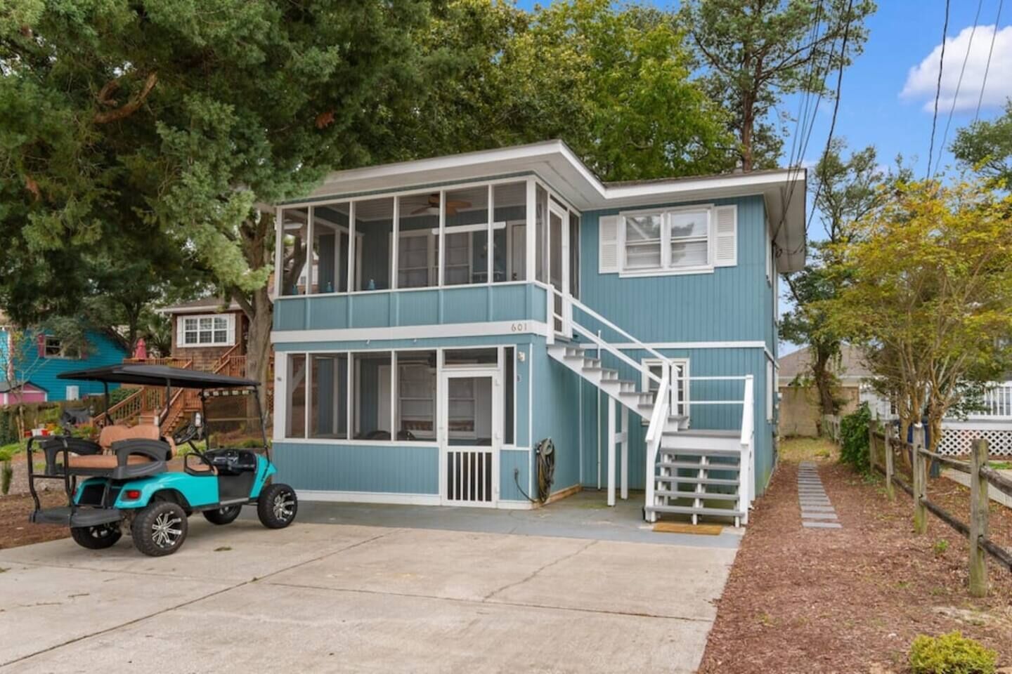 Una casa de dos pisos con fachada azul, un porche delantero y una escalera que conduce al nivel superior.