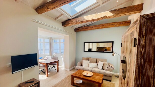 A modern living room with a flat-screen TV, a wooden coffee table, a sofa, and a large mirror reflecting a kitchen. - Apartment "Halbinsel Mönchgut" with Balcony and Wi-Fi (Binz)