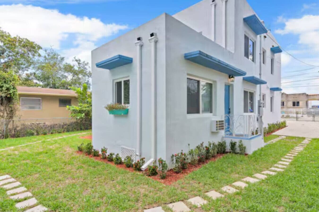 Une maison moderne à deux étages, dotée d’un toit plat, d’un petit porche et d’une pelouse bien entretenue.