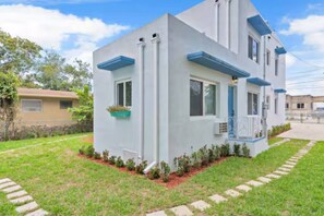 A modern two-story house with a flat roof, a small porch, and a well-maintained lawn. - Tropical Haven | Cozy 1 BR Caribbean Getaway (Miami)