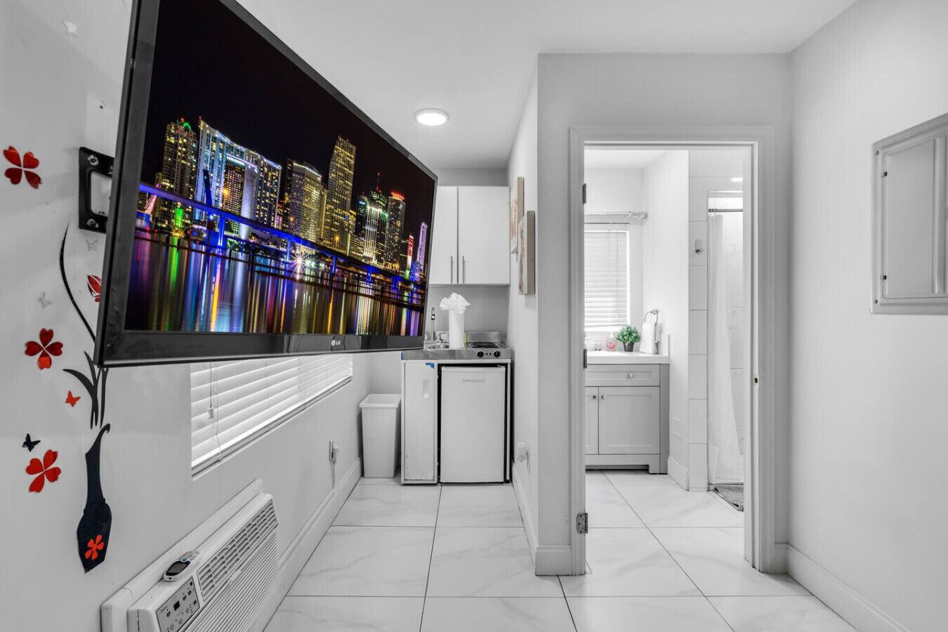A modern kitchen with a built-in LG TV displaying a cityscape, white cabinetry, and a small refrigerator.