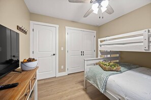 Une chambre avec un lit superposé, un bureau sur lequel se trouve un panier de fruits et un ventilateur de plafond.