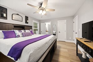 Une chambre à coucher avec un lit, un ventilateur de plafond, une télévision et une porte.