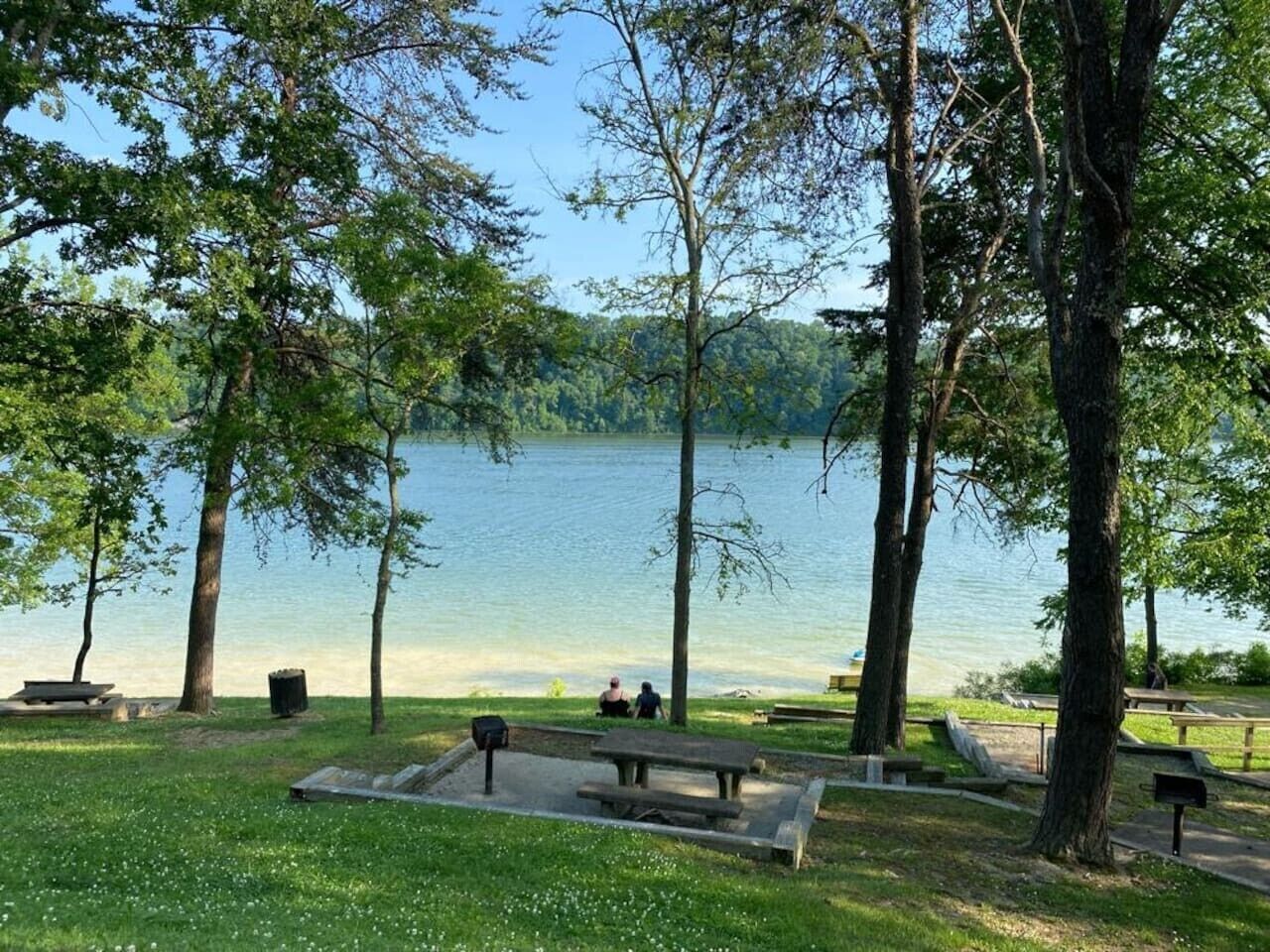 Un parc au bord du lac, doté de tables de pique-nique et de bancs, et entouré d’arbres.