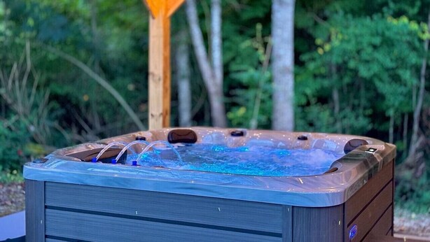 Un bain à remous installé sous une pergola en bois, illuminé de guirlandes lumineuses, et entouré de verdure.