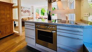 Une cuisine moderne dotée d’un four encastré, d’une hotte en acier inoxydable et d’un grand îlot central avec un plan de travail en verre.