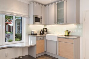 Una cocina moderna con muebles blancos, microondas integrado, cafetera y hervidor sobre la encimera.