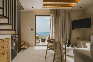 A modern living room with a view of the sea, a flat-screen TV mounted on the wall, and a staircase leading to an upper level. - Orizontas Suites 1 Syvota (Igoumenitsa)