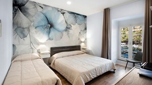 Ein Hotelzimmer mit zwei Betten, einer großen Blumenmalerei, Blick ins Freie und einem Schreibtisch mit Stuhl.