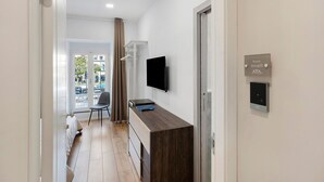 Ein Hotelzimmer mit Holzschreibtisch, Flachbildfernseher, einem Sessel, einem Kleiderschrank und einer Tür mit einer Zimmernummer.