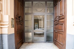 Une porte à deux battants en bois, dotée de panneaux en verre dépoli, d’une poignée en métal et d’une petite fenêtre circulaire située au-dessus.