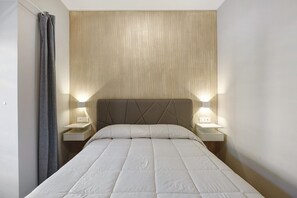 Un lit bien fait, avec une tête de lit, deux tables de chevet avec des lampes et un rideau sur le côté gauche.