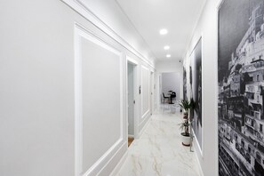 Un couloir aux murs blancs, doté d’un sol en marbre et orné d’une grande fresque représentant un paysage urbain en noir et blanc.