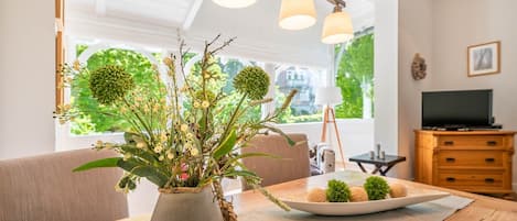 Et spiseområde med en vase blomster, en tallerken med dekorative genstande, et fjernsyn og et træskab.