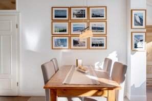 A dining area with a wooden table and chairs, a central light fixture, and a wall adorned with framed photographs. - Apartment 'Die Stubnitz' with Winter Garden and Balcony Effect (Binz)
