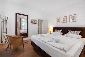 A hotel room with a large bed, a chair, a bedside table with a lamp, and a door leading to another room. - Apartment 'Die Stubnitz' with Winter Garden and Balcony Effect (Binz)
