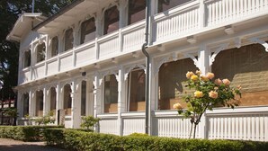 Um edifício branco com várias janelas e varandas, rodeado por vegetação.