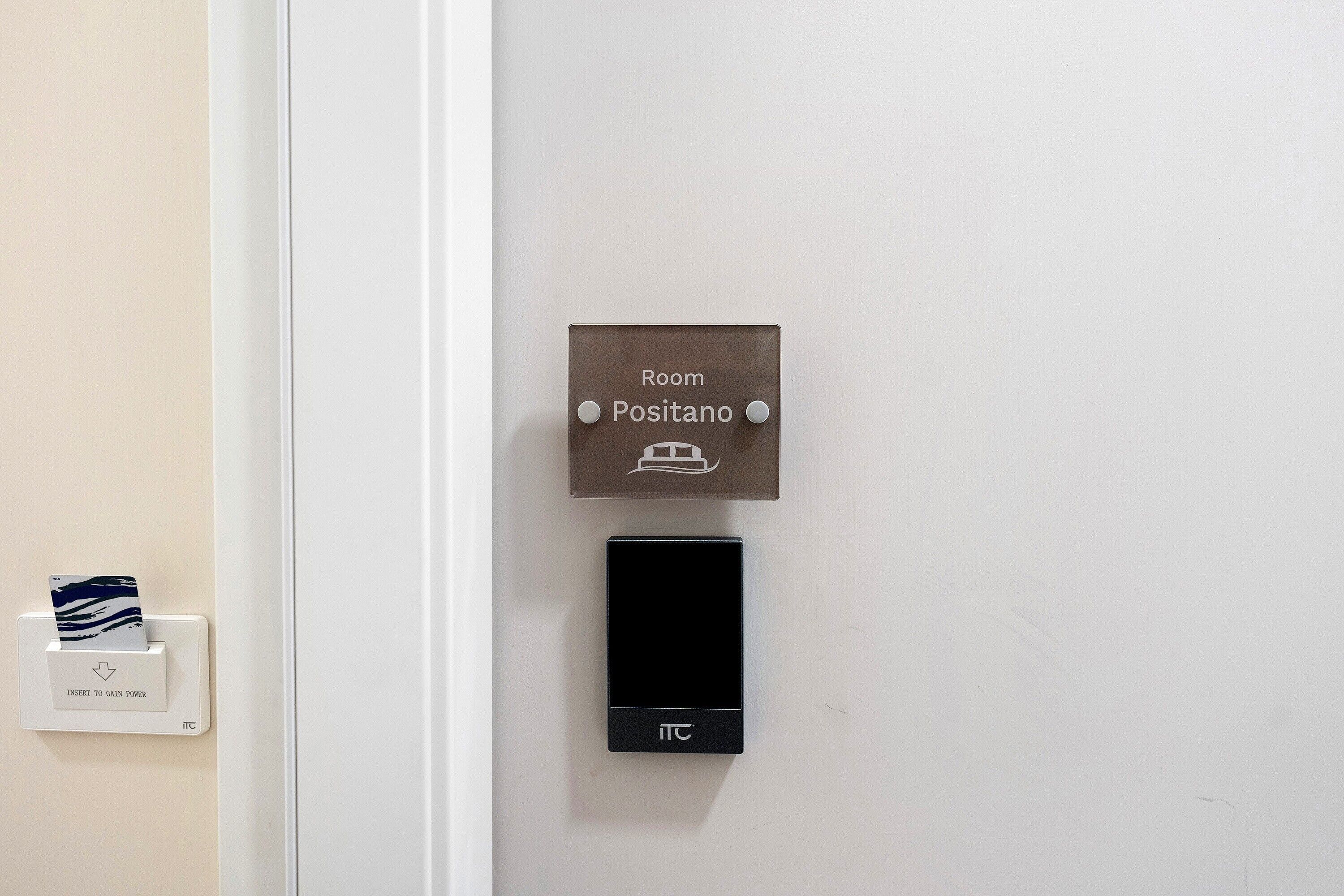 A hotel room door with a sign indicating 'Room Positano' and a power outlet with a card reader.