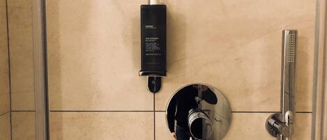 A bathroom with a shower, a wall-mounted soap dispenser, and a round mirror.