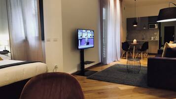 Ein modernes Hotelzimmer mit Bett, Fernseher, Sofa, Essbereich und Küchenzeile.