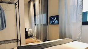 A hotel room with a bed, a TV mounted on the wall, a wardrobe, and a small table with a lamp. - Palazzina B  (Genoa)
