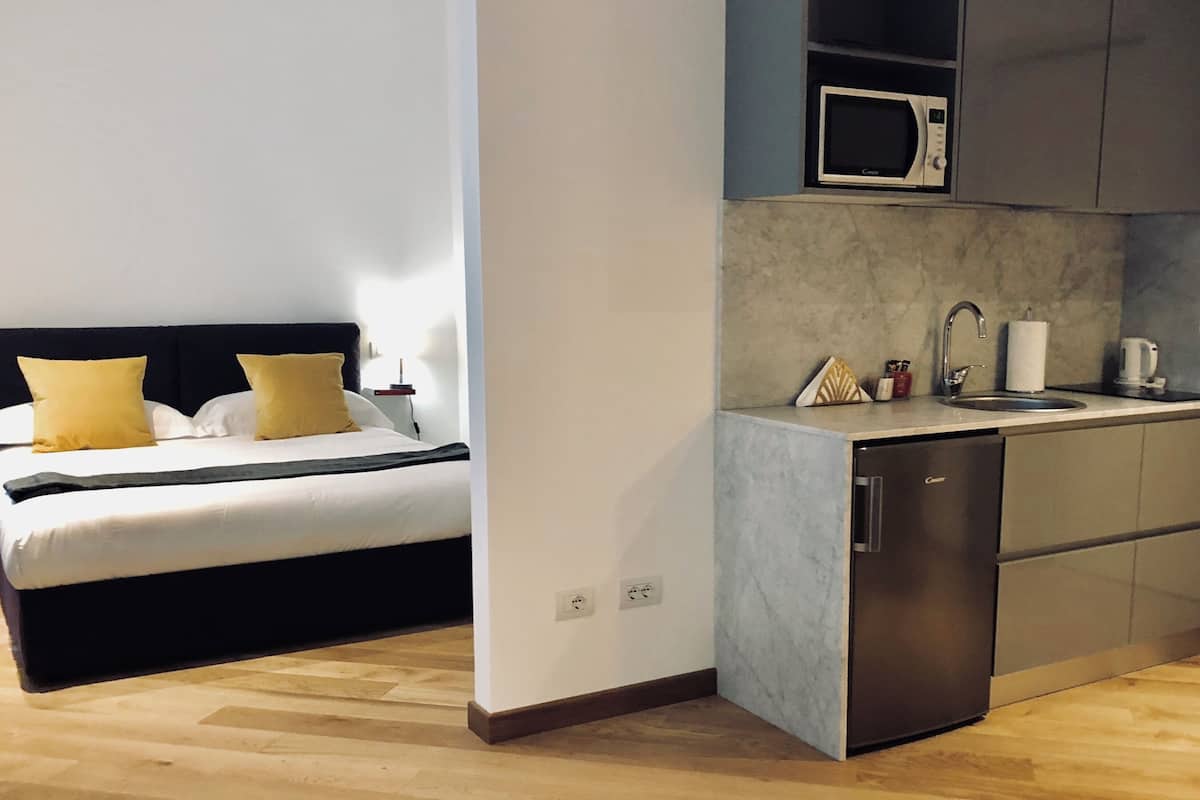 A compact hotel room with a bed, bedside table, and a small kitchenette including a microwave and sink.