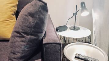 A dark gray sofa with a yellow pillow, a white round side table with a black lamp, and a remote control on the table.