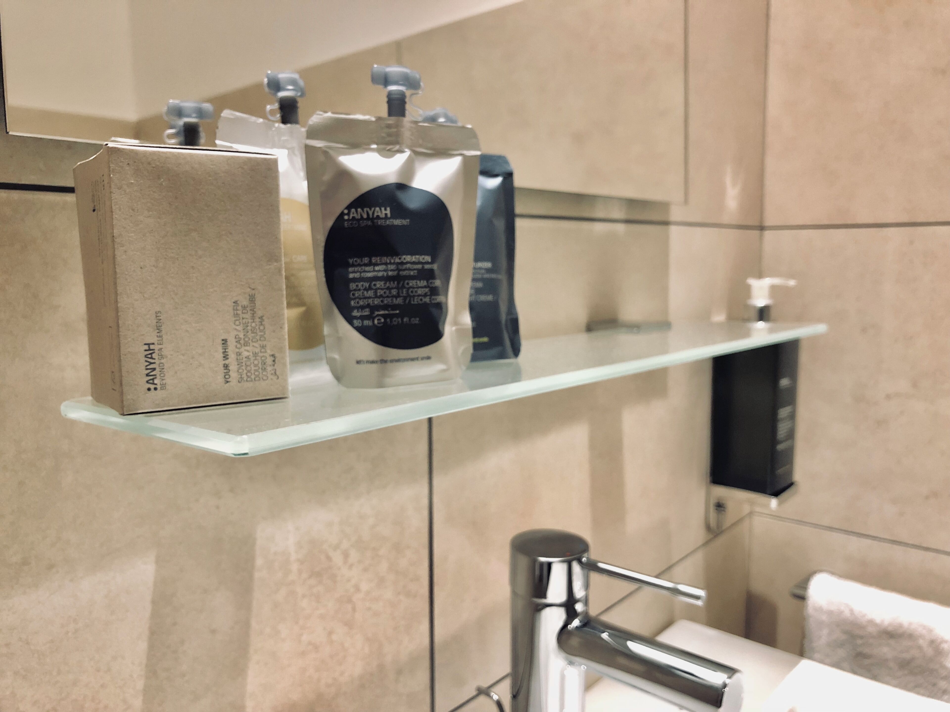 A bathroom with a glass shelf holding a box labeled 'ANYAH' and two bottles of body cream.