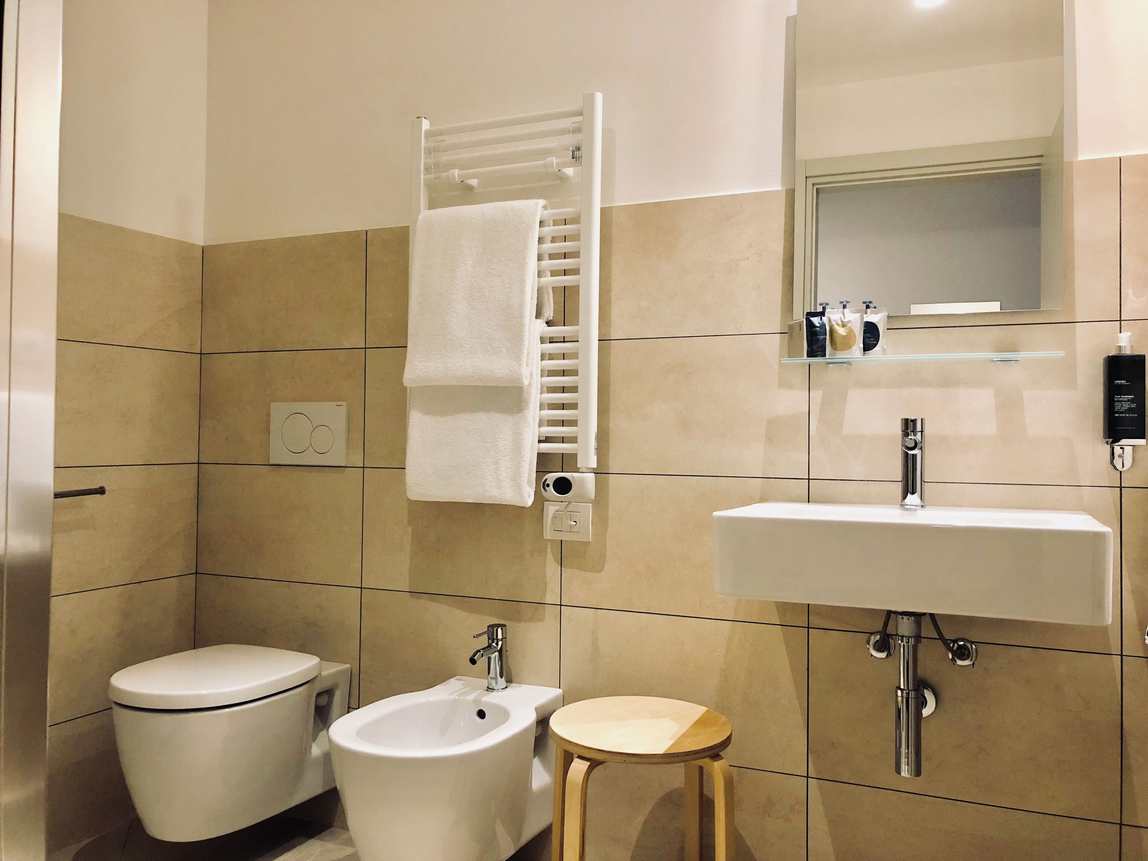 A modern bathroom with a toilet, bidet, sink, and a small stool.