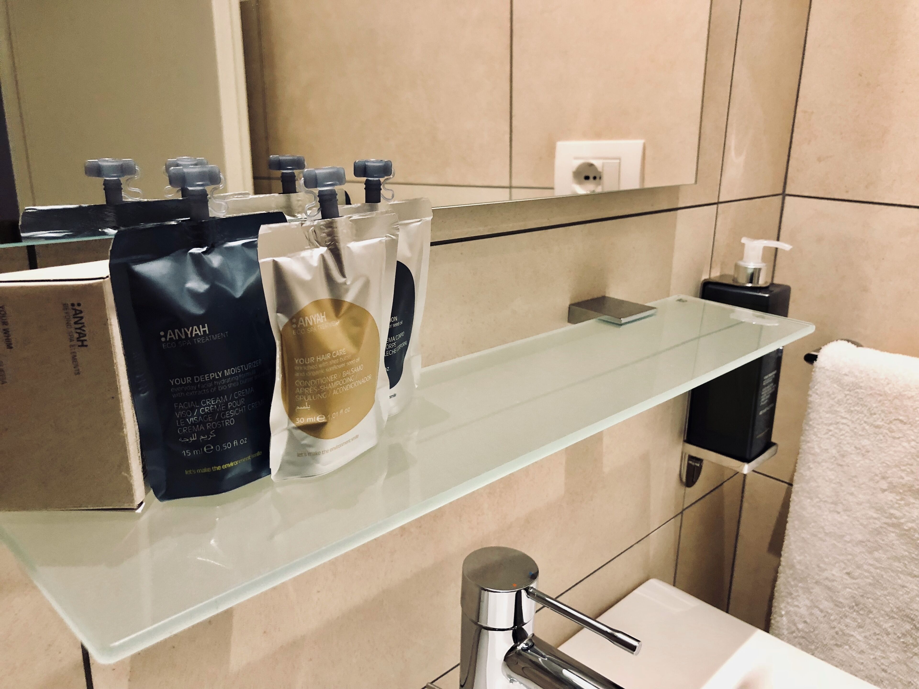 Une salle de bain avec une étagère en verre où sont rangés les articles de toilette, un porte-serviettes et un miroir.