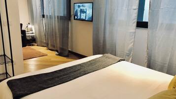 A hotel room with a bed, a TV mounted on the wall, a desk with a chair, and a window with curtains.