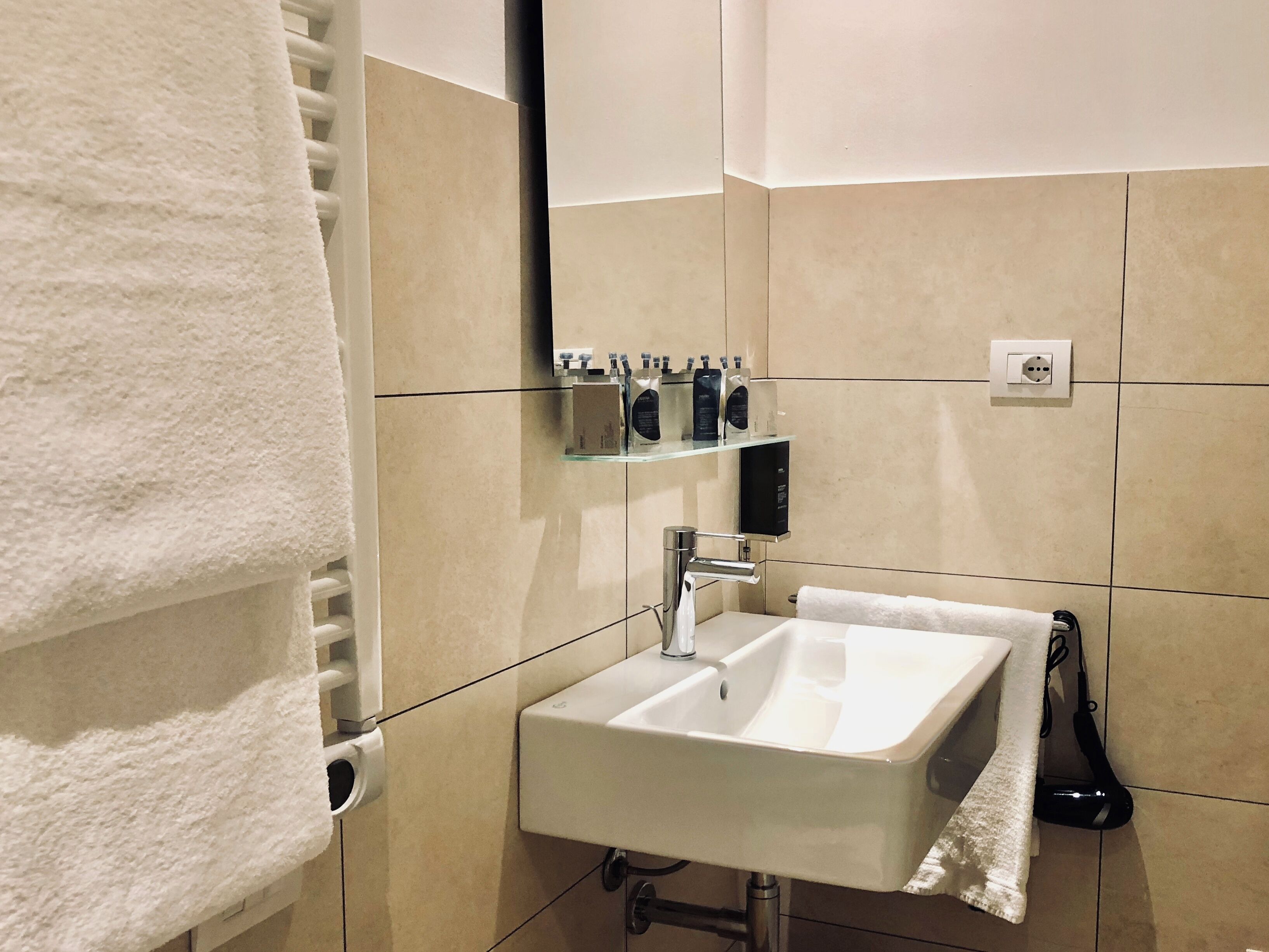 A bathroom with a white sink, a towel rack, a mirror, and a shelf with toiletries.