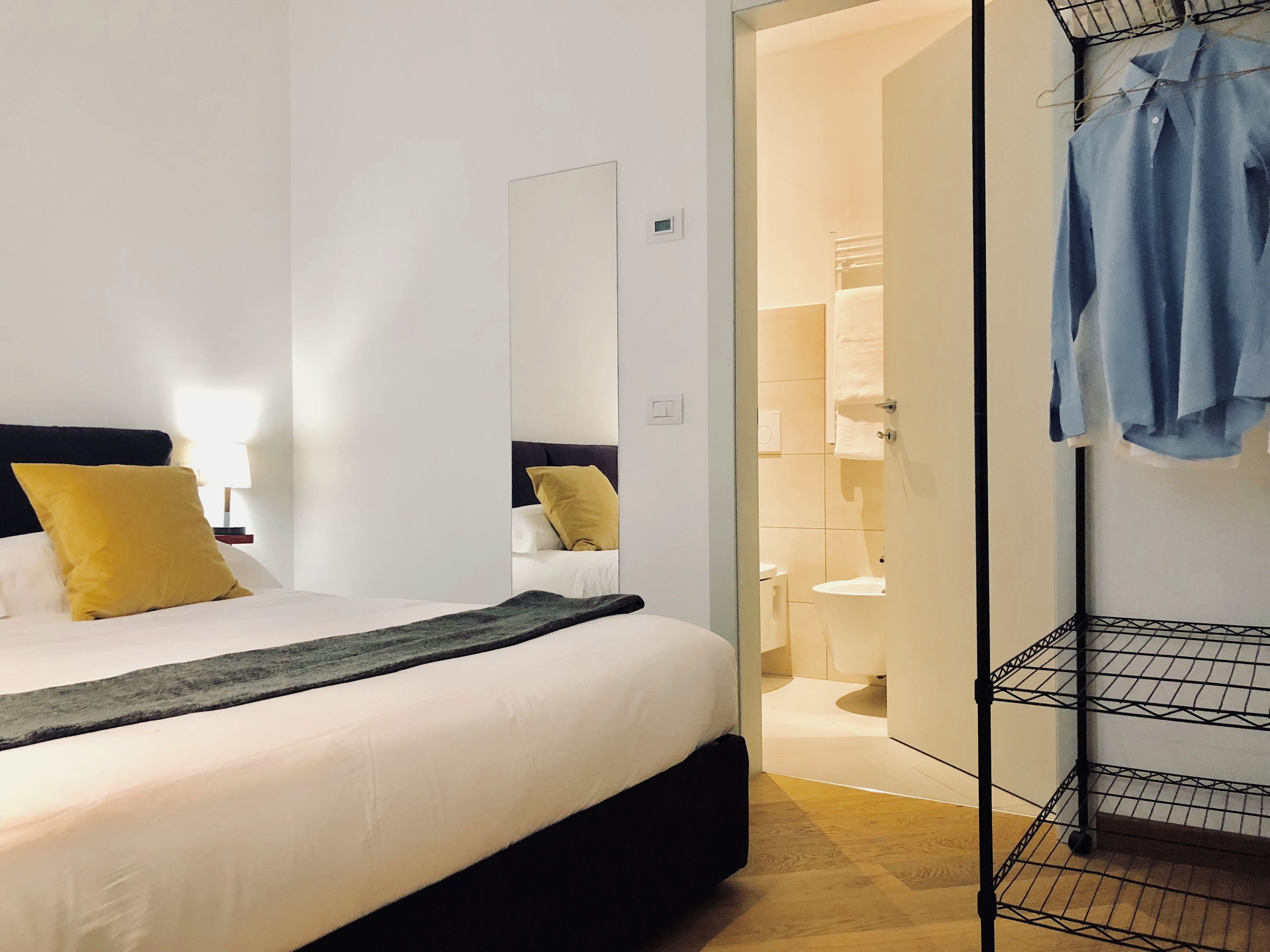 Una habitación de hotel moderna con una cama, un espejo, un armario y un baño visible a través de una puerta abierta.