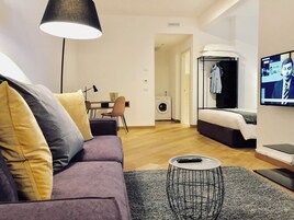 Una sala de estar moderna con un sofá morado, una mesita redonda y un televisor montado en la pared.