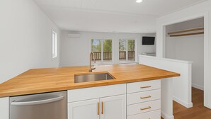 A modern kitchen with a wooden countertop, stainless steel sink, and white cabinetry.