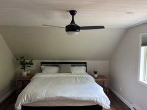 A bedroom with a bed, a ceiling fan, a nightstand with a plant, and a window.