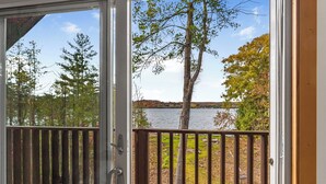 A view from a sliding glass door to a deck with a wooden railing overlooking a lake and trees.